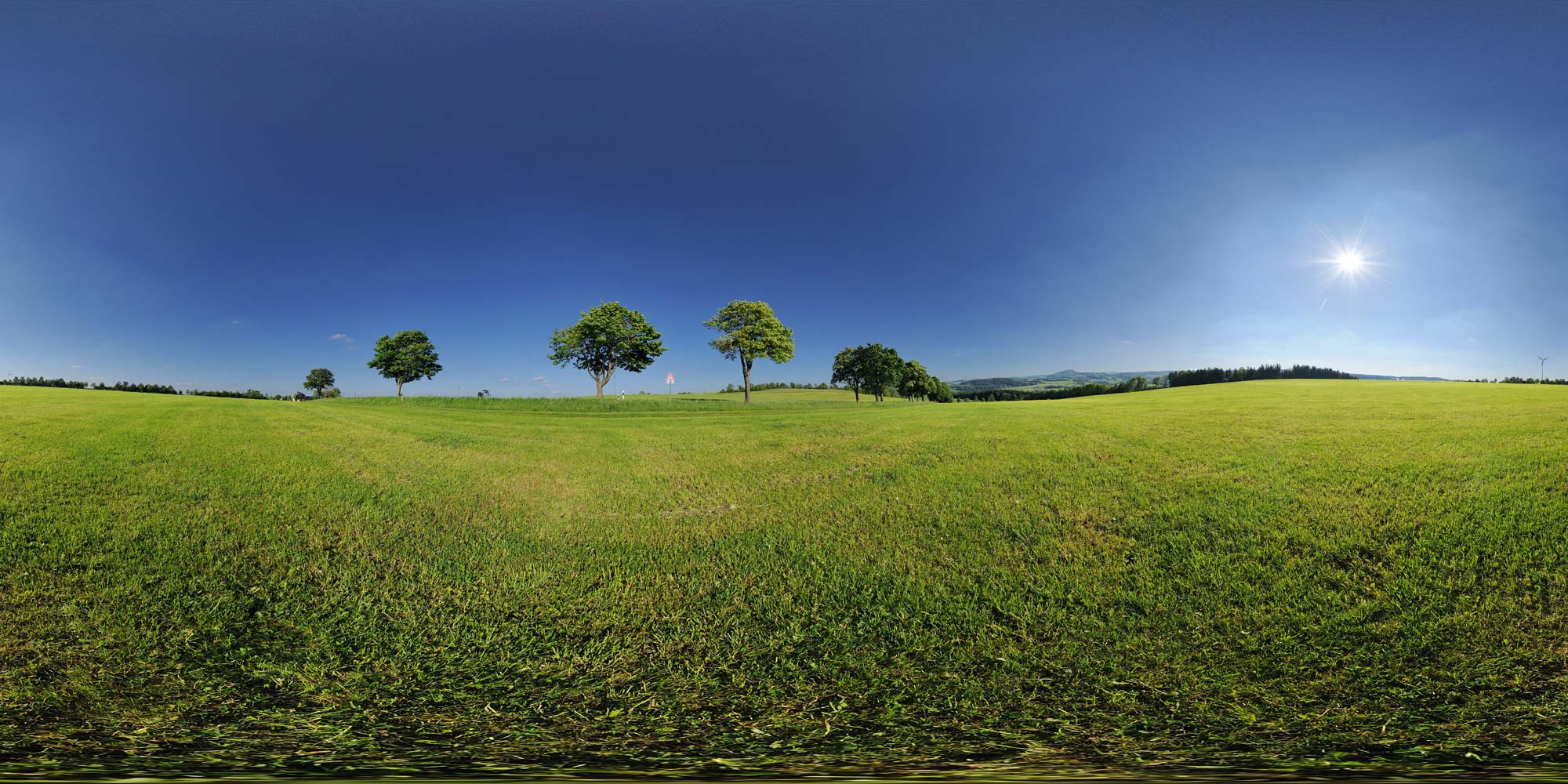 Eine weite, grüne Hügellandschaft unter strahlend blauem Himmel lädt zu entspannten Wanderungen ein.