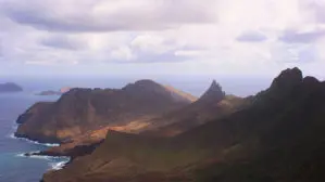 Blick über die karge und kantige Küste der Robinson Crusoe Inseln bei Abendlicht und leicht bewölktem Himmel