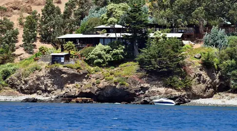 Blick vom Boot aus auf die Robinson Crusoe Lodge, die an einem Felshang liegt.