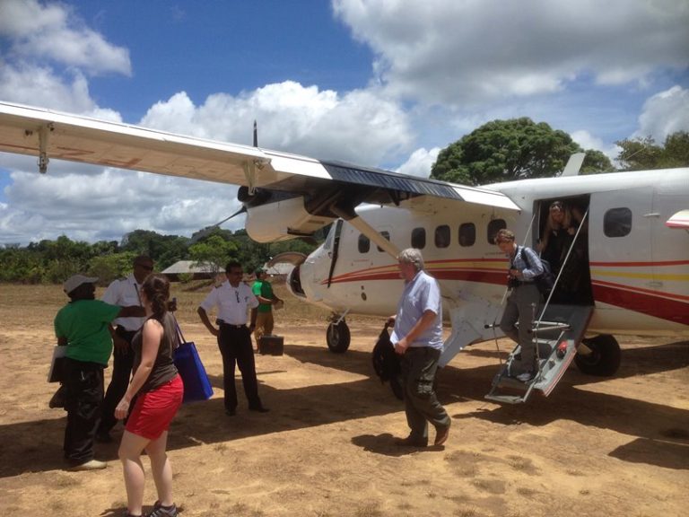 Reisende steigen aus einem kleinen Propellerflugzeug auf einer Landebahn im dichten Dschungel aus