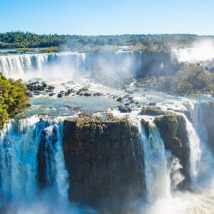 Blick auf die rauschenden Iguazu Wasserfälle bei strahlendem Sonnenschein.