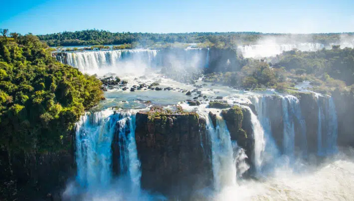 Blick auf die rauschenden Iguazu Wasserfälle bei strahlendem Sonnenschein.