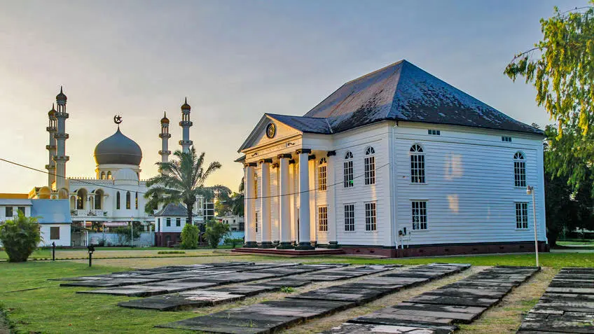 Im Vordergrund steht die Synagoge, aus weißem Holz in holländisch-kolonialem Stil gebaut. Im Hintergrund, nur einige Meter entfernt ragt die Moschee mit seinen vie Minaretten auf.