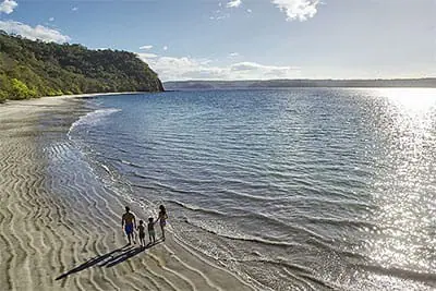 Eine langgezogene Bucht bei Abendstimmung im Norden Costa Ricas. Eine Familie mit zwei Kindern geht direkt am Strand spazieren.