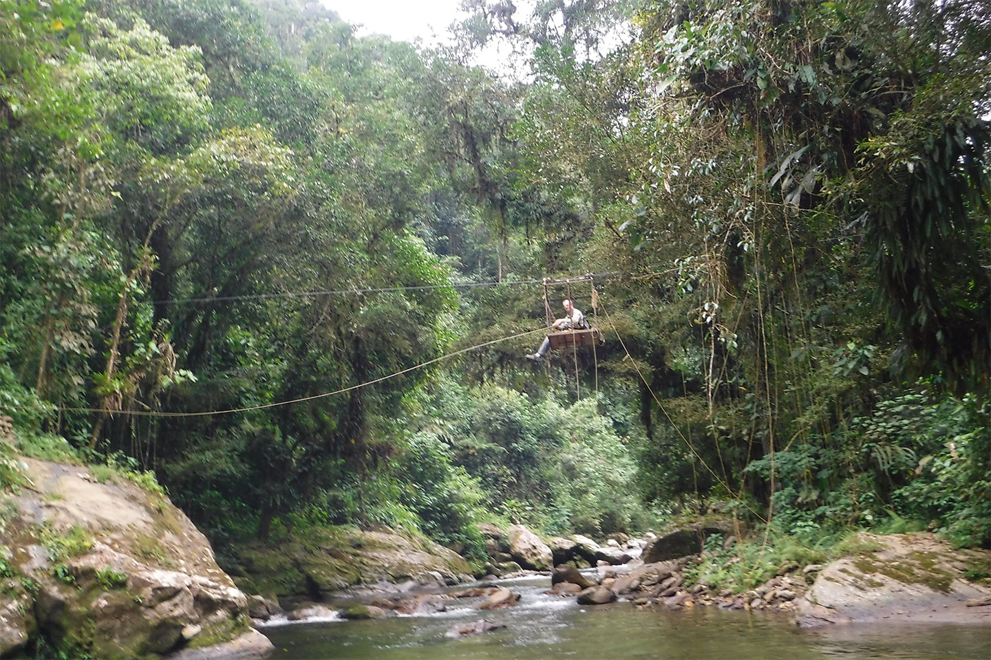 Person in einer kleinen Seilgondel über einem Fluss im dichten Dschungel während des Trekkings zur Ciudad Perdida in Kolumbien.