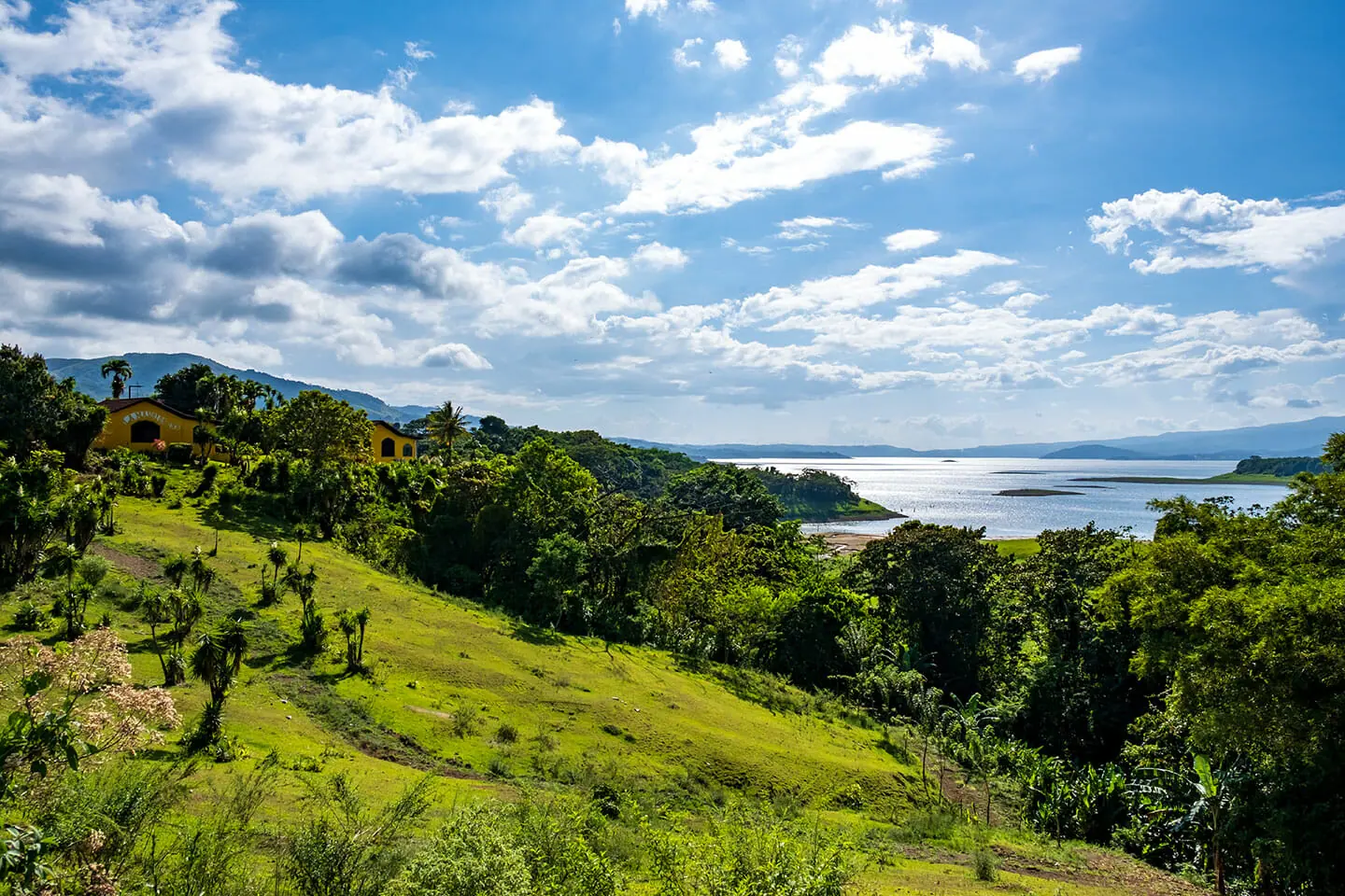 Der Arenalsee in Costa Rica, umgeben von Hügeln und Regenwald, unter leicht bewölktem Himmel.