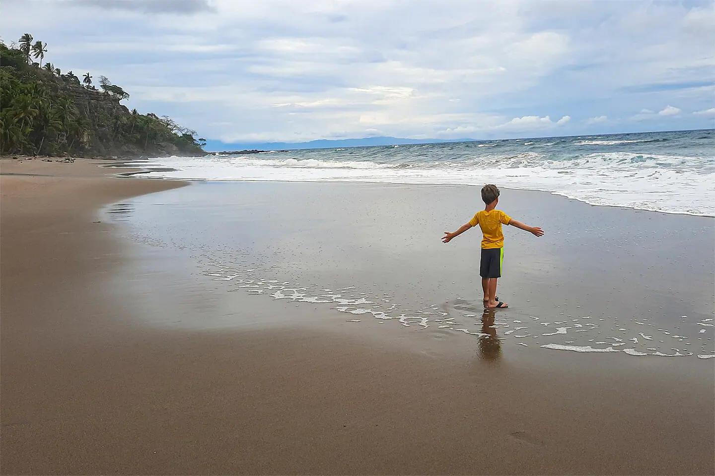 Ein kleiner Junge am Playa Tambor, unter einem bewölkten Himmel.
