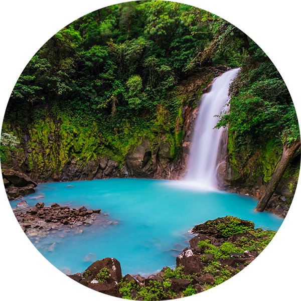 Eine steinige Bucht, in der ein Wasserfall in das türkisfarbende Wasser des Rio Celeste fällt.