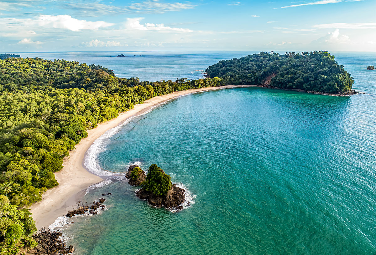 Blick aus der Vogelperspektive auf den Playa Espadilla Sur, einem der schönsten Strände des Manuel Antonio Nationalparks. Der Strand zieht sich bogenförmig bis zu einer Halbinsel. Dicht am Strand beginnt der Regenwald.