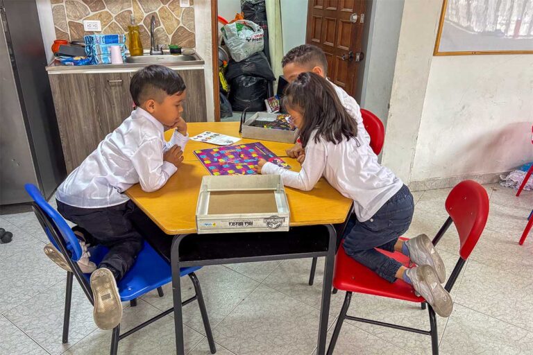 Szene in der Einrichtung von Hogar de Paz: Drei Kinder sitzen um einen Tisch herum und spielen