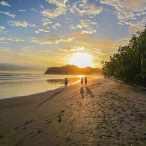Ein Strand in Costa Rica bei Sonnenuntergang. Drei Menschen gehen spazieren.