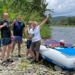 Ein Gruppenbild der Reisenden, die mit Napur Tours nach Costa Rica gereist sind. Sie stehen vor einem Schlauchboot am Flussrand und winken zur Kamera.