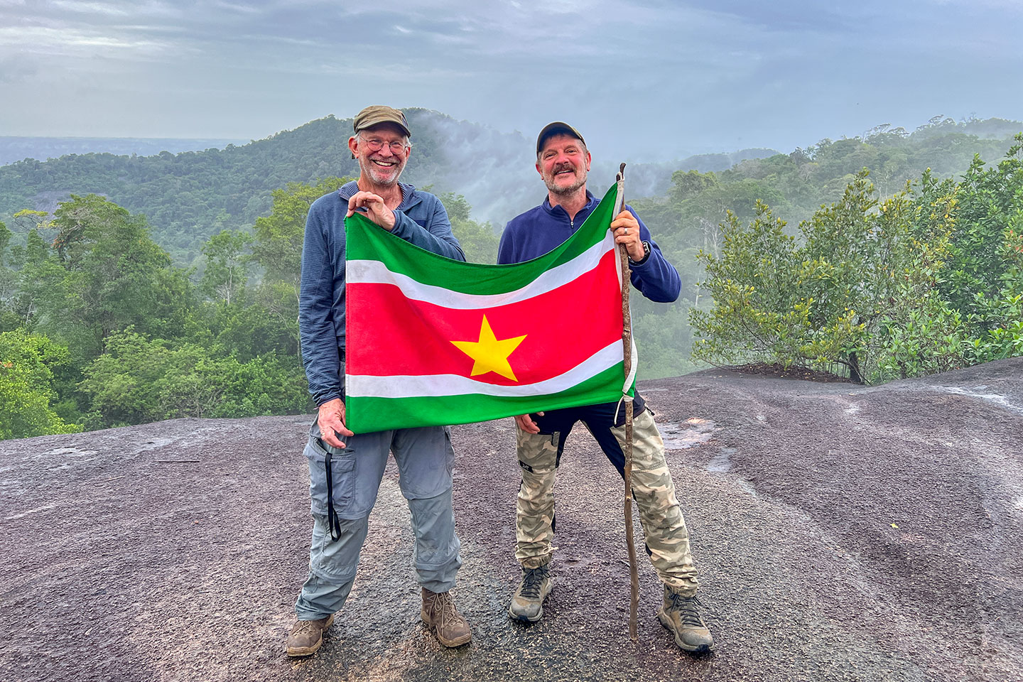 Uwe Zündorf steht mit seinem Freund auf dem Fredberg. Sie halten eine Fahne von Suriname in der Hand. 