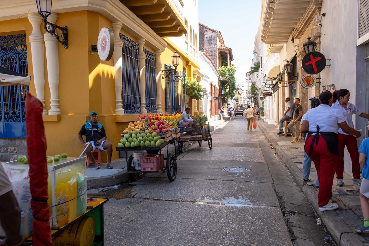 Eine Straße in der Altstadt von Cartagena. Ein Mann sitzt vor einem Karren, darauf verschiedenes Obst