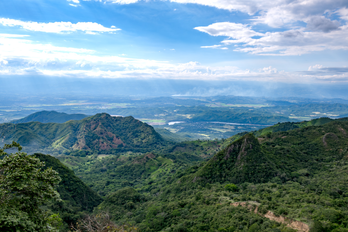 Weitläufige Berg- und Tallandschaft der kolumbianischen Anden mit grünen Hügeln, Flusstälern und weiter Ebene im Hintergrund, aufgenommen während einer Mietwagenreise durch Kolumbien.