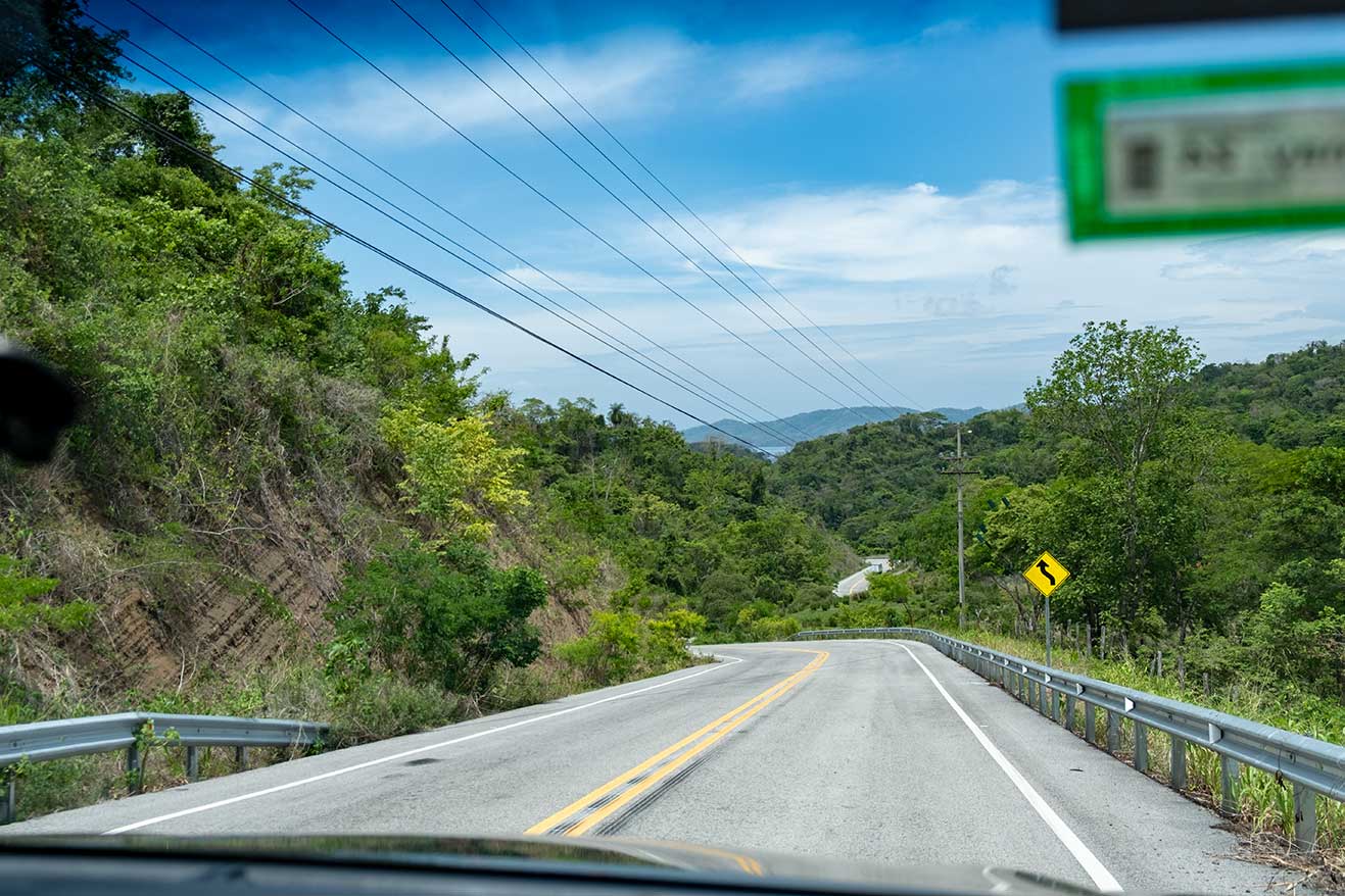 Blick aus dem Auto: Eine Straße führt kurvenreich durch grüne Lsndschaft Costa Ricas.