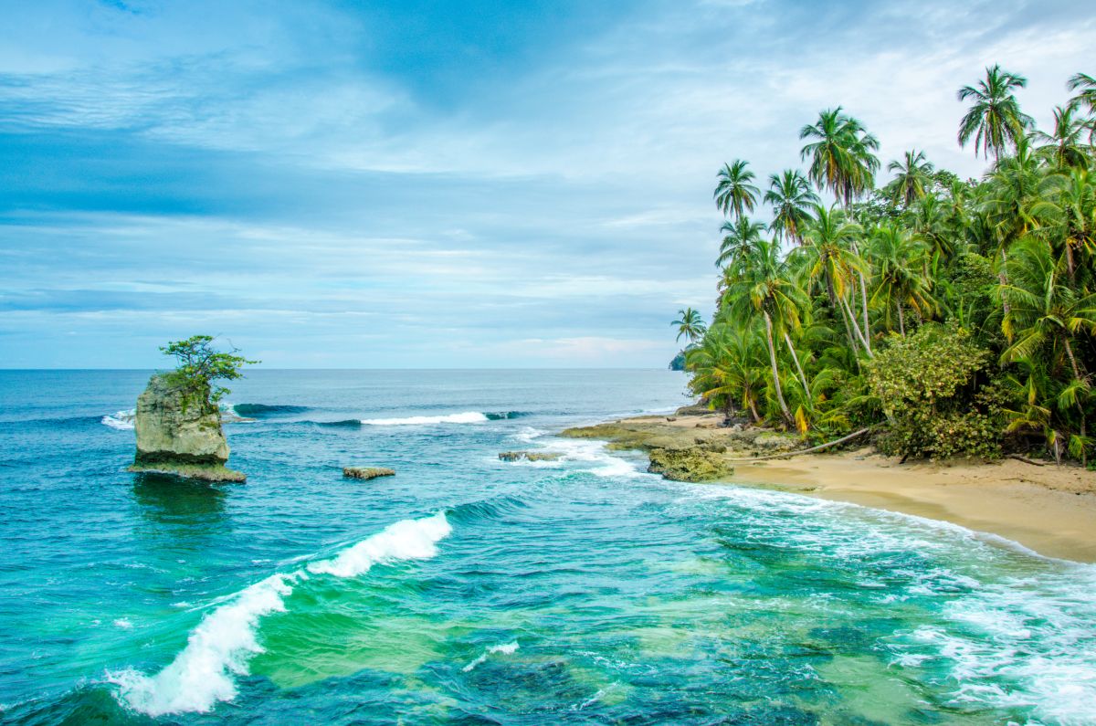 Ein tropischer Sandstrand mit Palmen und einer markanten Felsformation im türkisfarbenen Meer in Costa Rica.