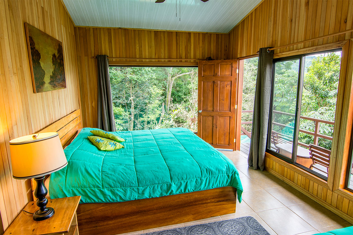 Helles Gästezimmer der Cala Lodge in Monteverde mit Doppelbett, großen Fenstern und offener Tür zur Terrasse mit Blick in den umliegenden Regenwald.