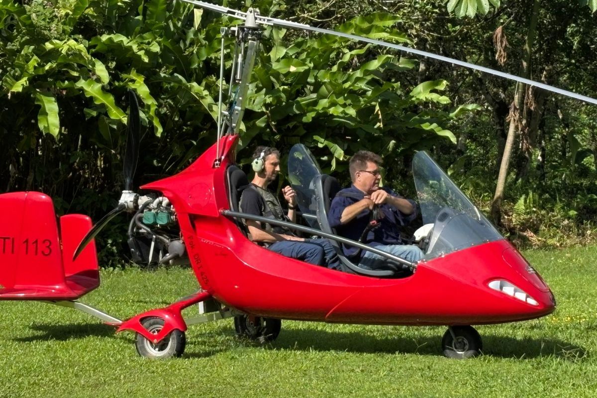 Zwei Männer sitzen in einem roten Tragschrauber auf einer Wiese vor tropischer Vegetation während einer Reise in Costa Rica.