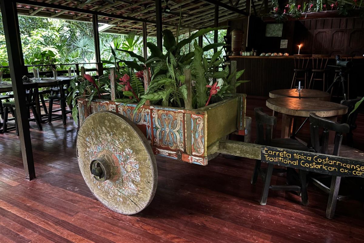 Ein bunt bemaltes traditionelles Ochsenkarren-Dekor mit Pflanzen steht im offen gestalteten Restaurantbereich einer Lodge während einer Rundreise in Costa Rica.