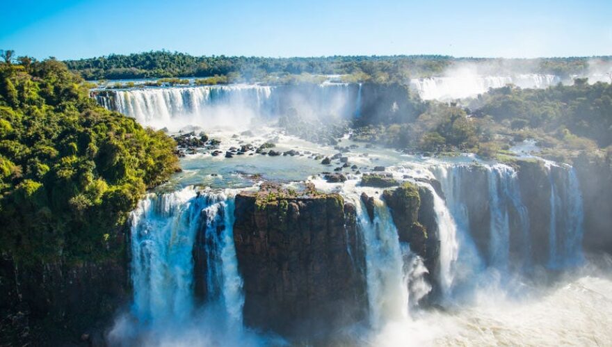 Blick auf die rauschenden Iguazu Wasserfälle bei strahlendem Sonnenschein.